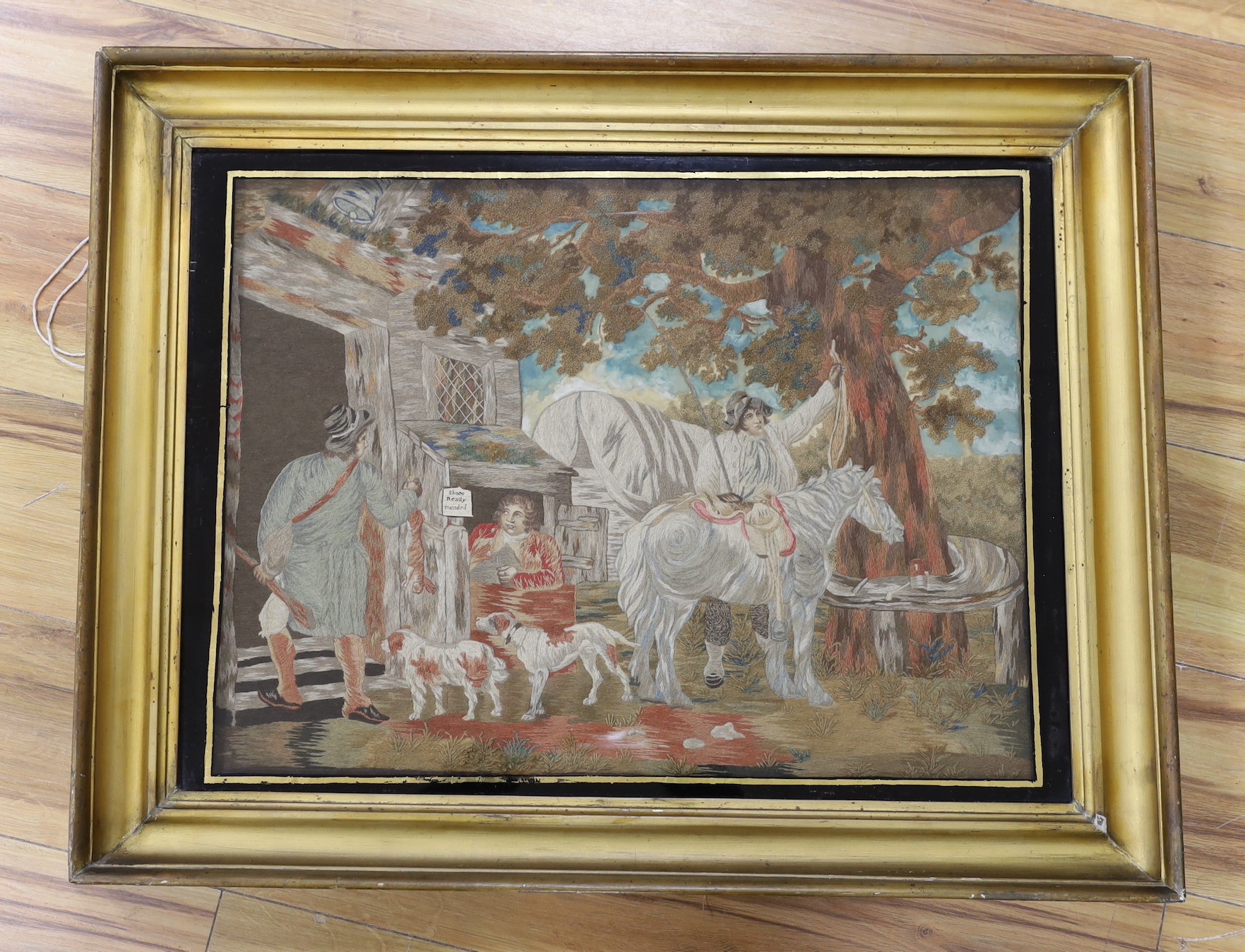 A late Georgian silkwork picture of a shoe repair shop, 44 x 59cm